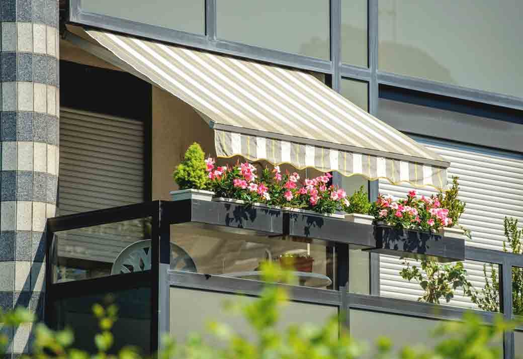 Balcony with striped awning, flower boxes with pink flowers, and glass railings.