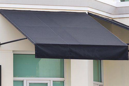 Black awning over a window on a white building, providing shade.