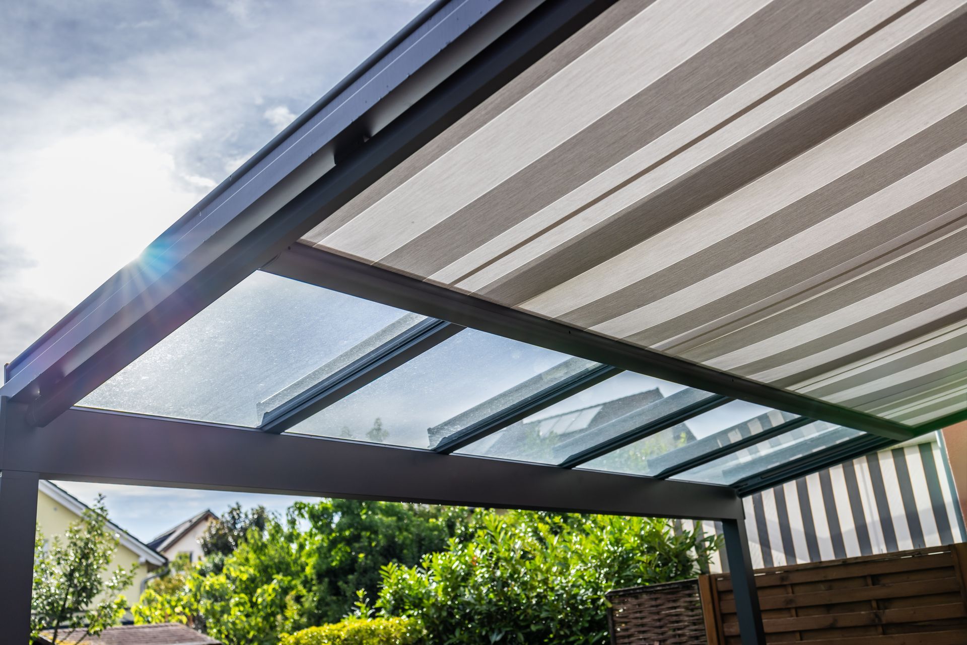 A modern pergola with a retractable striped awning and glass panels