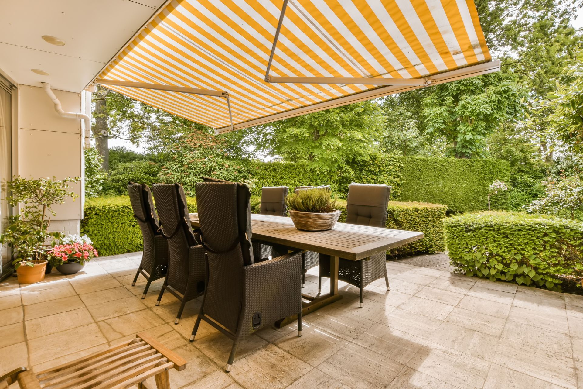 An outdoor dining area with a table and chairs under a yellow fabric-striped awning over the patio. An outdoor dining area with a table and chairs under a yellow fabric-striped awning over the patio.