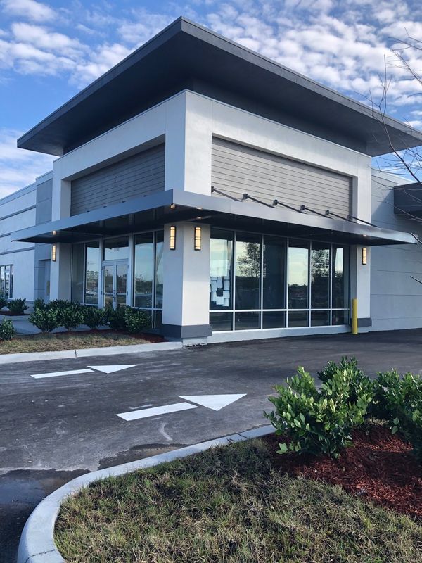 Modern building with large windows, grey awnings, and drive-up arrows on asphalt.