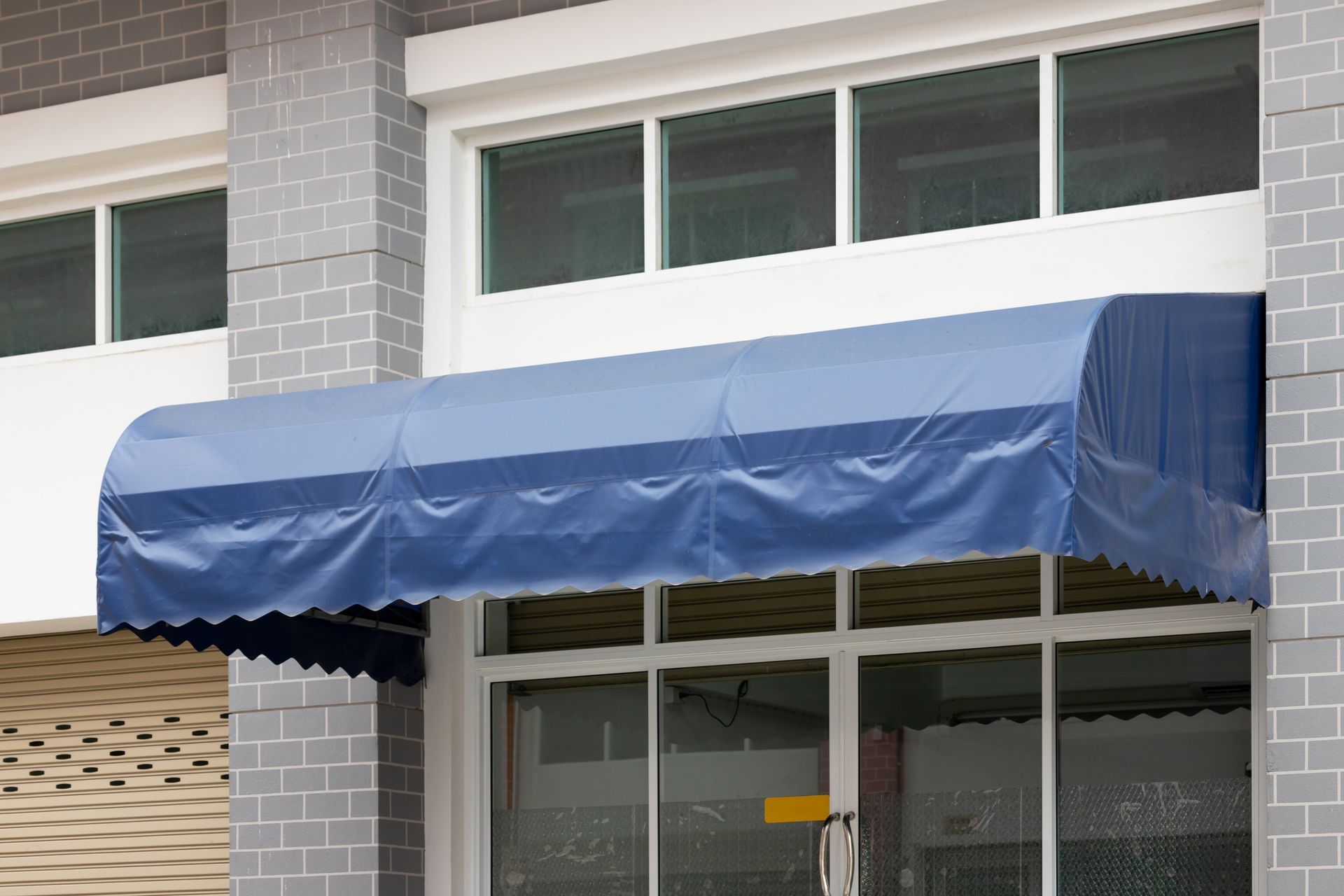 Blue awning over a storefront window. The building has a white window frame and gray brick.