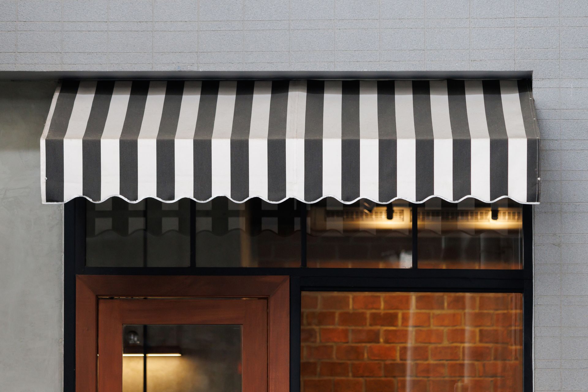 Black and white striped awning above a glass window and wood door on a gray brick building.