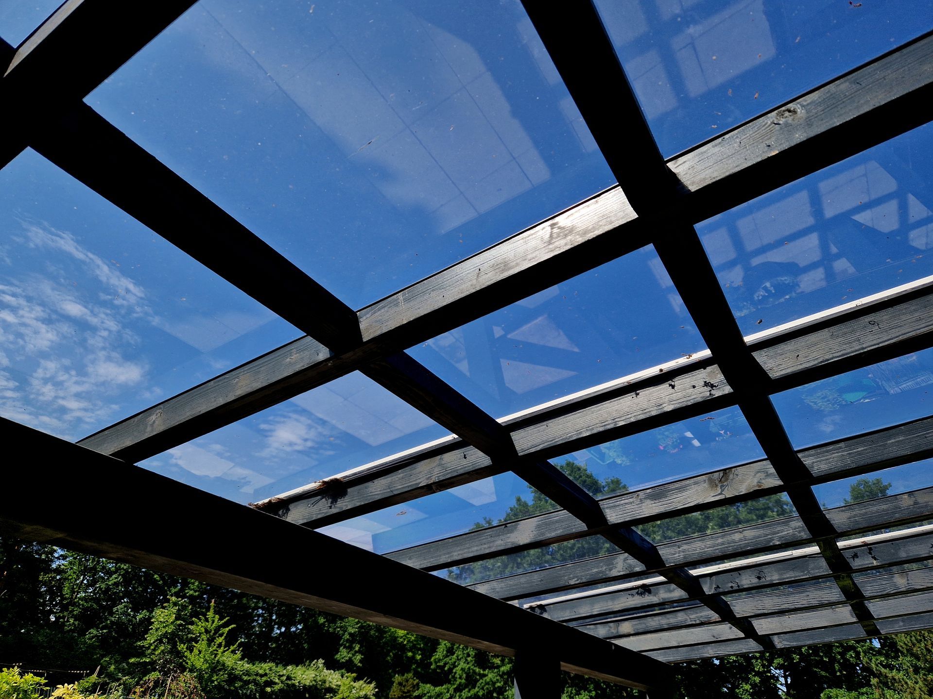 Black wooden pergola with translucent panels, blue sky visible.