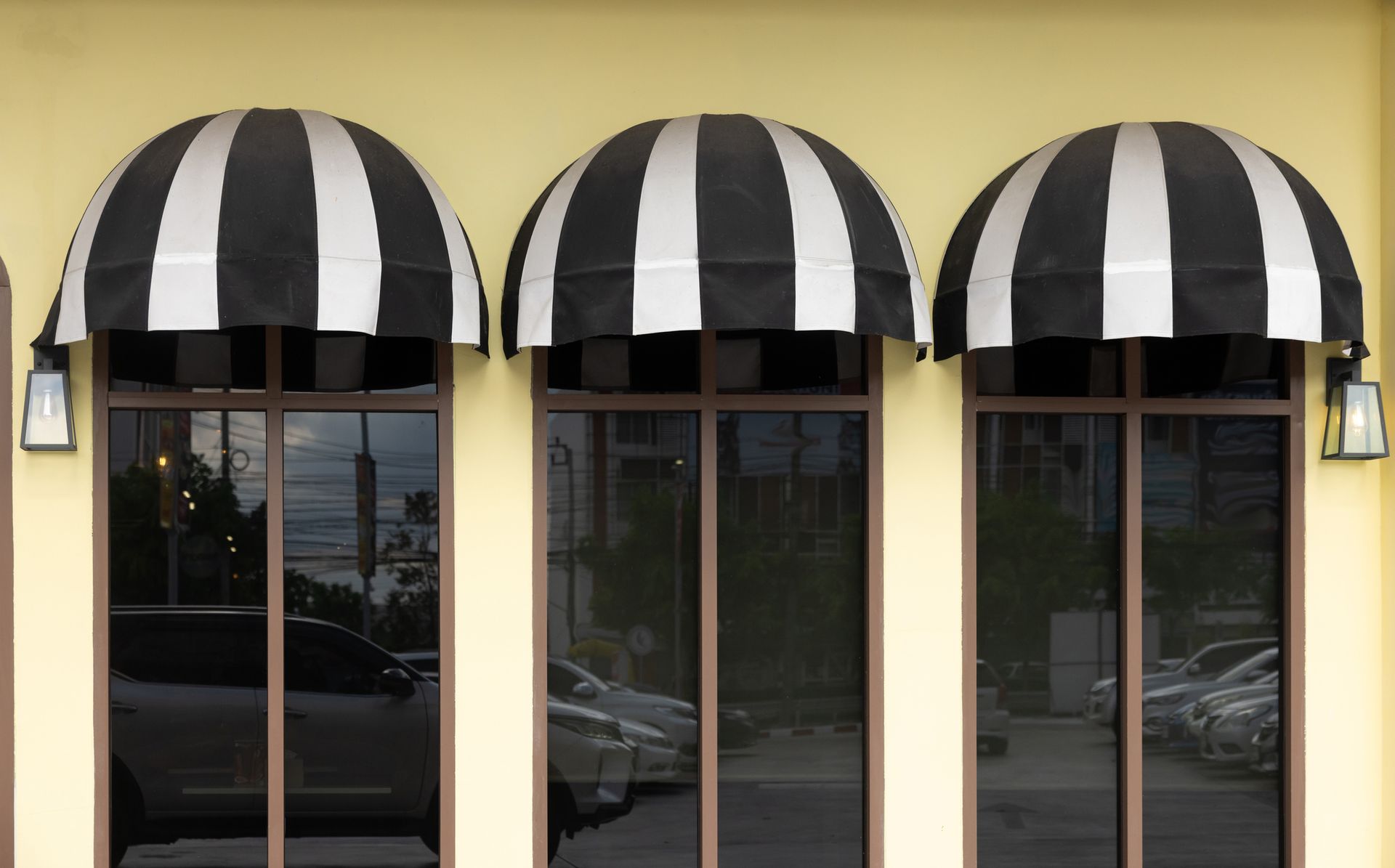 Three arched windows with black and white striped awnings, brown frames, and reflections of cars.