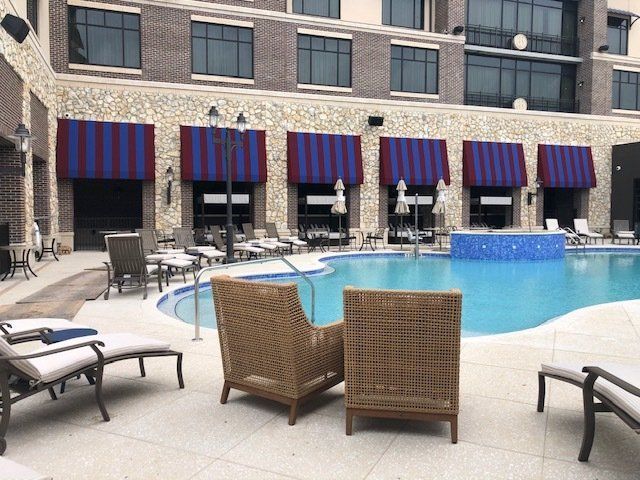 Poolside patio with striped awnings, chairs, and a pool in front of a brick building.