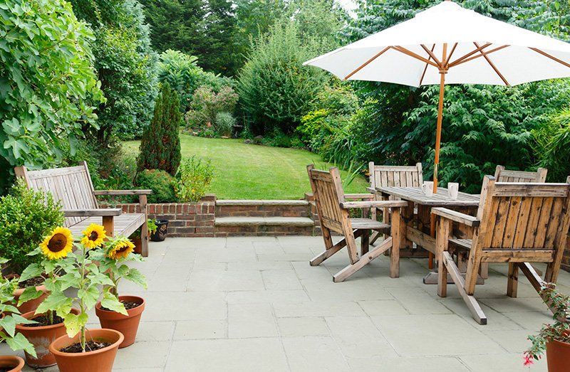 Patio with wooden furniture, parasol, potted sunflowers, and a lush green lawn.