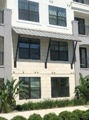 Modern building facade with metal awning over large windows and greenery. Modern building facade with metal awning over large windows and greenery.