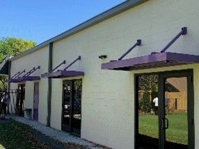 Light-colored building with purple metal awnings over glass doors. Light-colored building with purple metal awnings over glass doors.