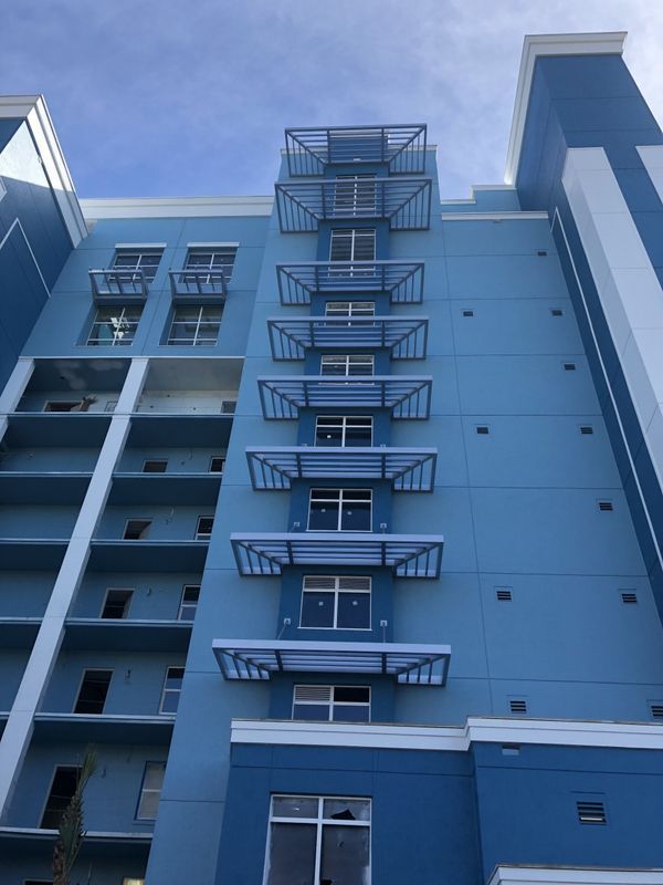 Blue building with a series of rectangular metal awnings. White trim and windows. Light blue sky in background.