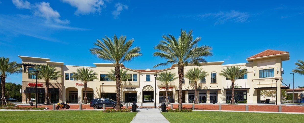 Palm trees in front of a cream-colored retail strip under a bright blue sky.