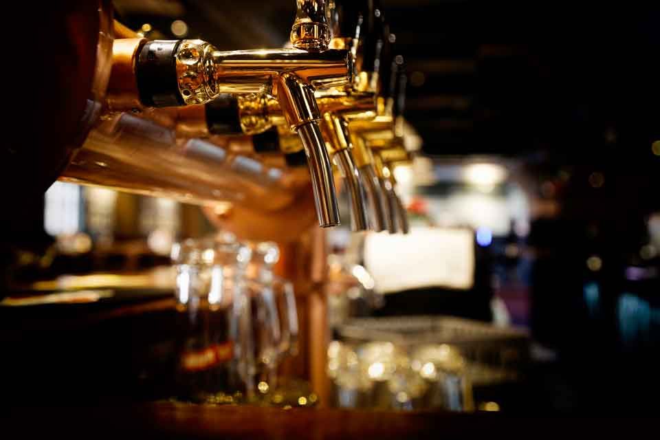 Close-up of golden beer taps in a bar, with glasses and blurred background.