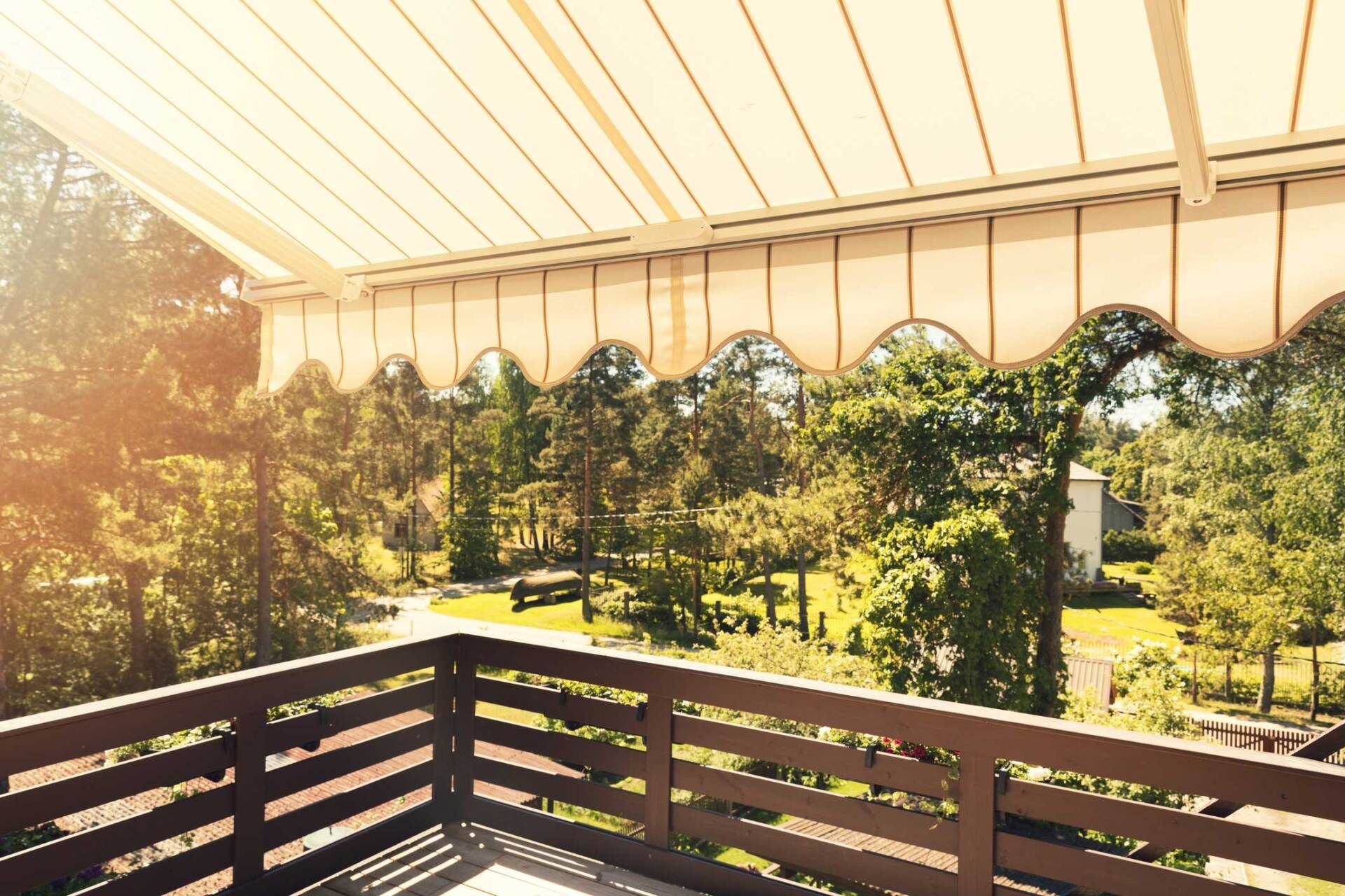Balcony overlooking trees with a beige awning, brown railing, and dappled sunlight.