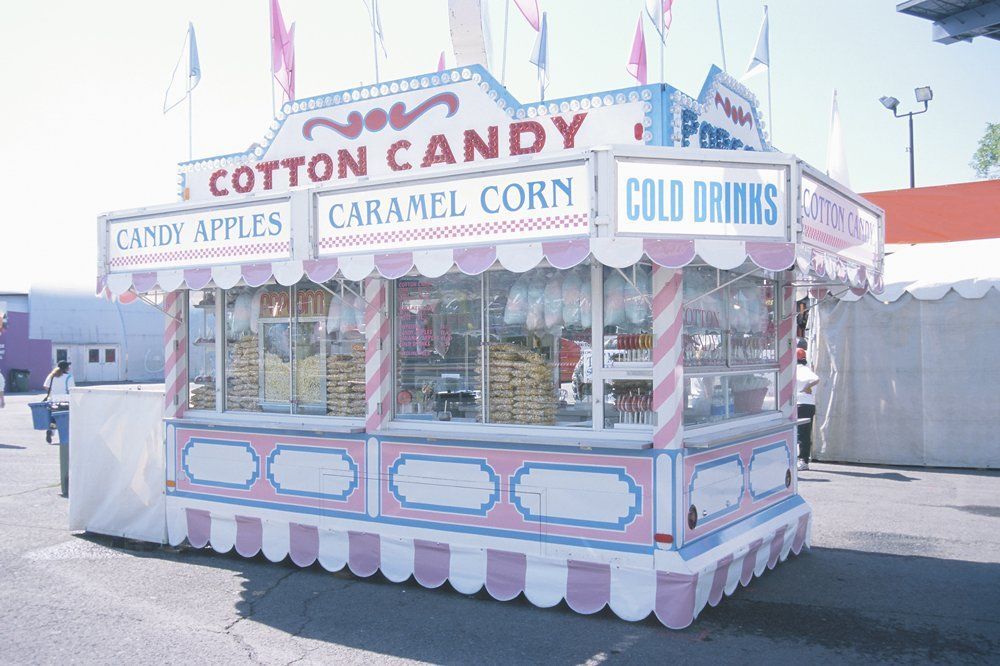 Cotton candy stand at a fair, with candy apples, caramel corn, and cold drinks for sale.