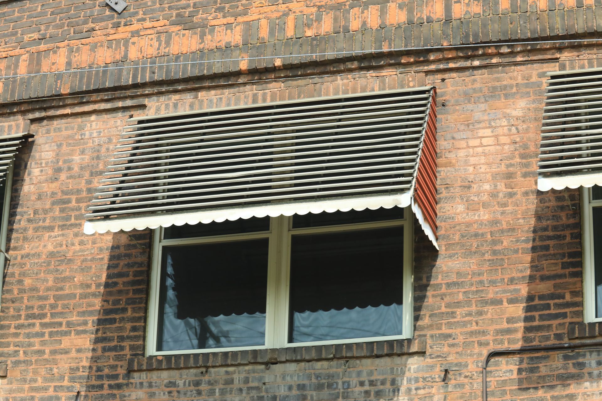 Brick building with a window covered by a decorative awning with scalloped edges.