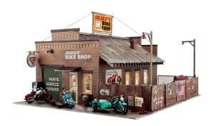 Vintage biker shop exterior with corrugated roof, motorcycles parked outside, and wooden fence signage.