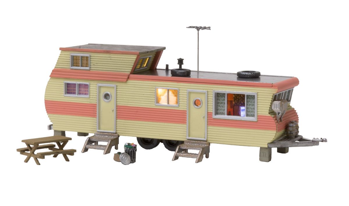 Toy camper trailer with tan and red stripes, lit windows, picnic tables, and a rooftop antenna on a white background