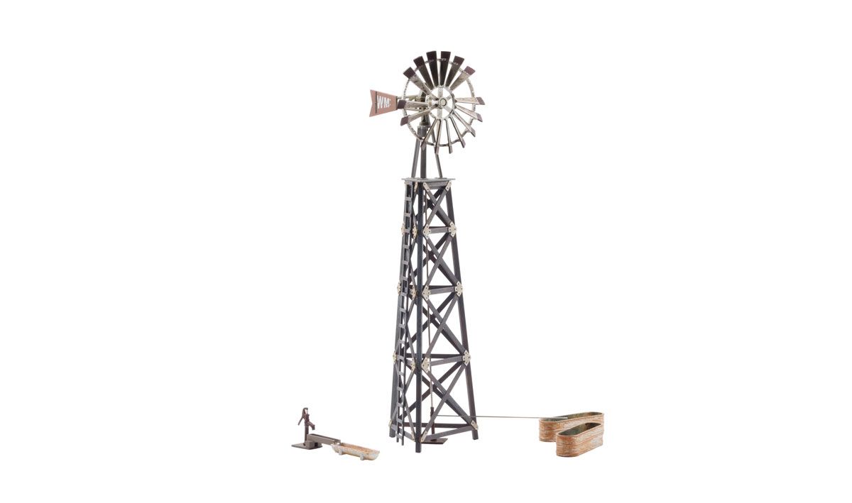 Rusty metal windmill tower with fan on white background, with small equipment pieces nearby