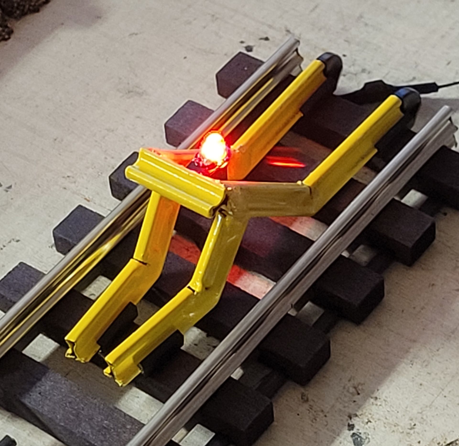 Yellow track-mounted robot on railroad tracks with a glowing red light
