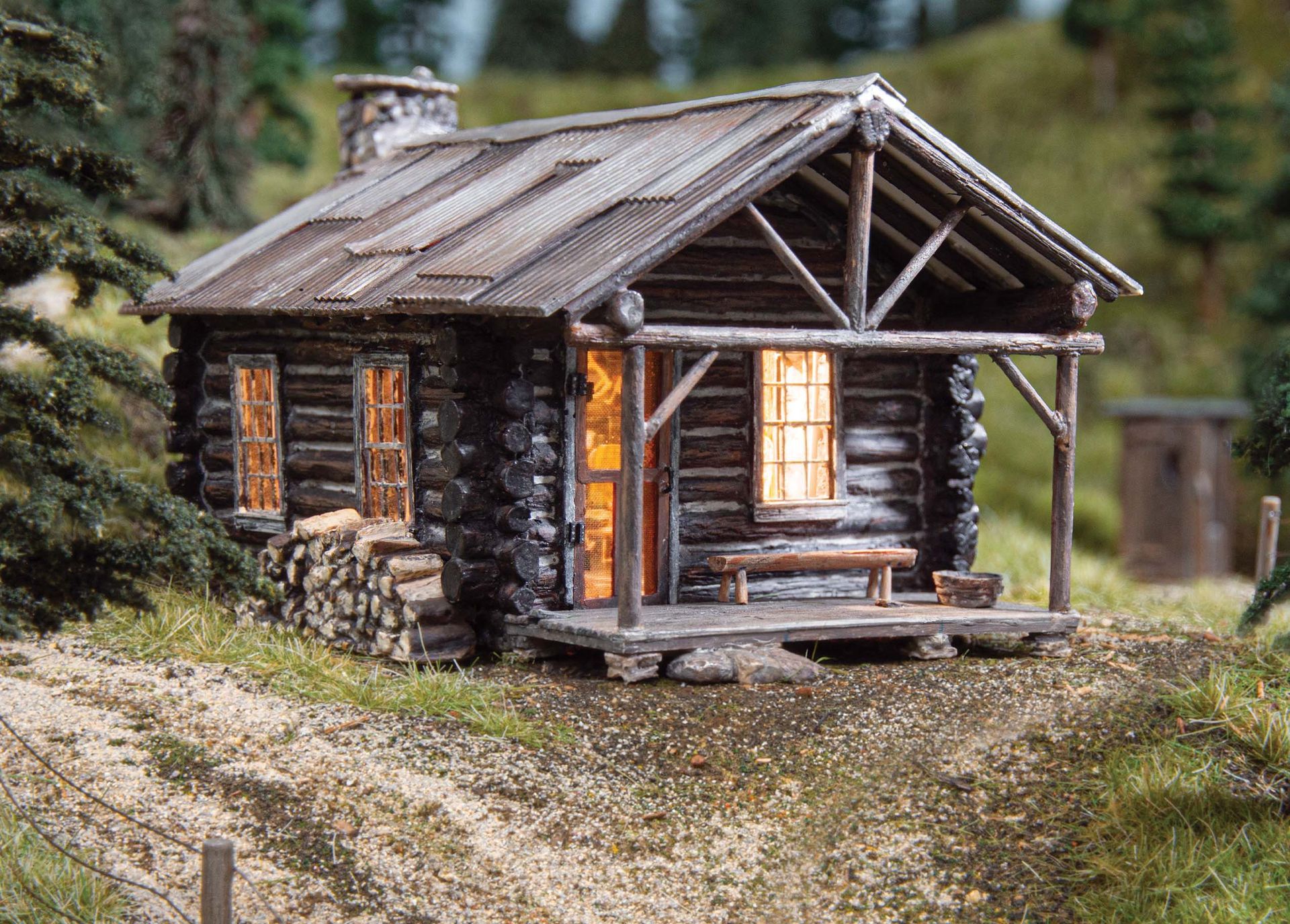 Miniature log cabin with glowing windows and a rustic porch on a grassy path