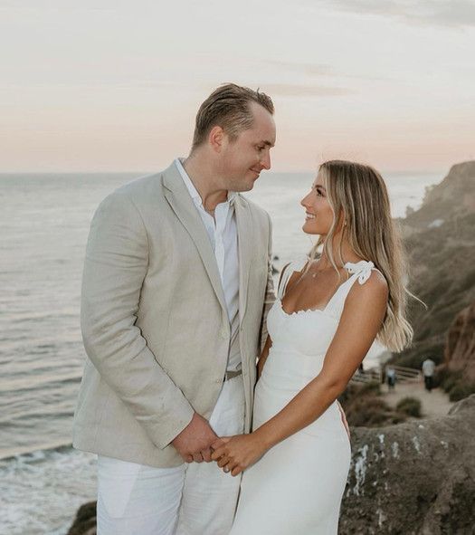 A bride and groom are standing next to each other on a cliff overlooking the ocean.