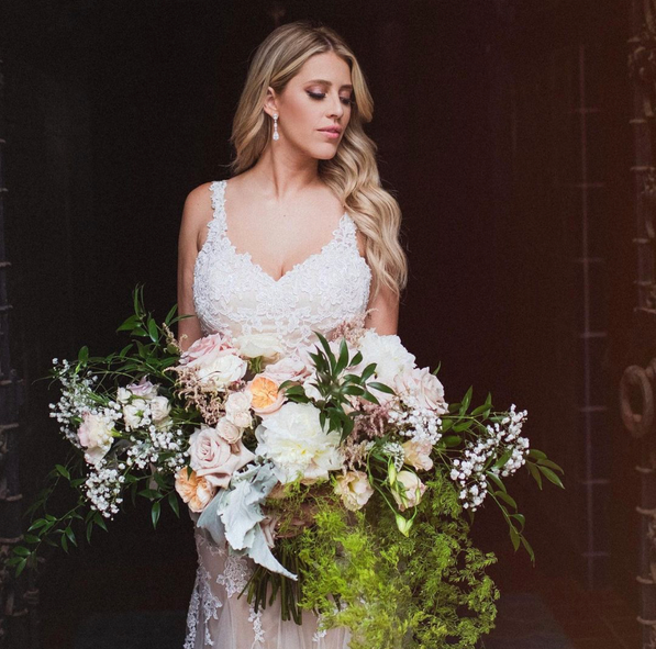 A woman in a wedding dress is holding a large bouquet of flowers.