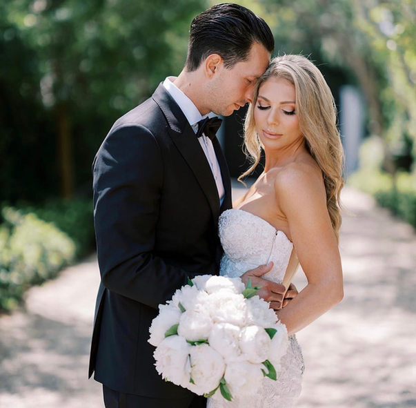 A bride and groom are posing for a picture and the bride is holding a bouquet of white flowers