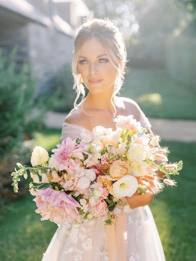 A bride in a wedding dress is holding a bouquet of pink and white flowers.