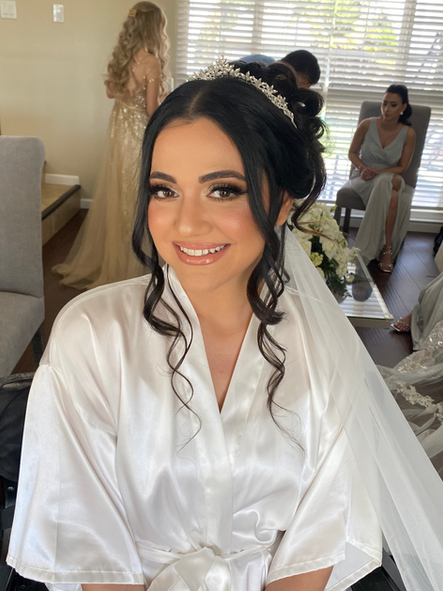 A woman in a white robe and veil is smiling while getting ready for her wedding.