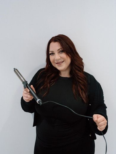 A woman in a black shirt is holding a curling iron.