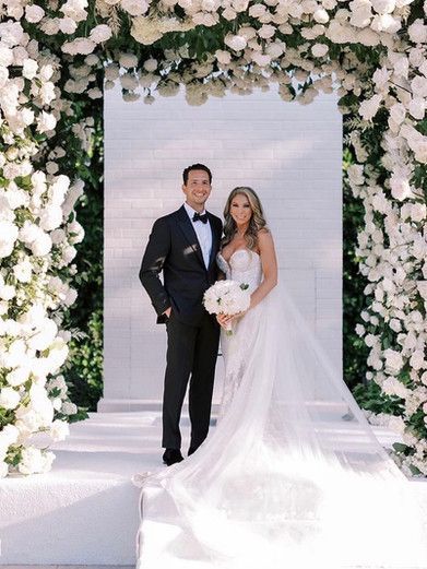 A bride and groom are posing for a picture in front of a floral arch.