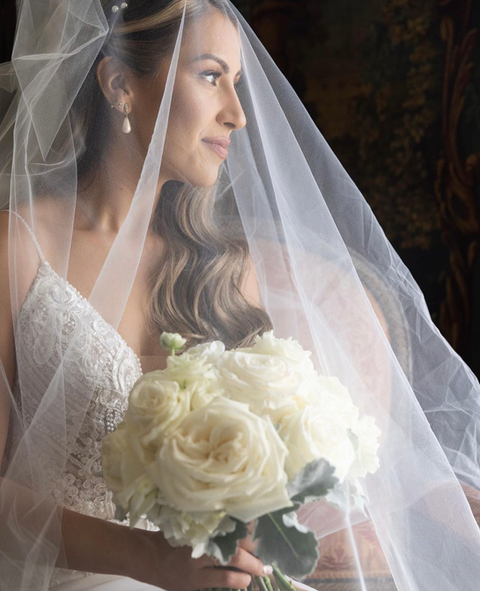 The bride is wearing a veil and holding a bouquet of white roses