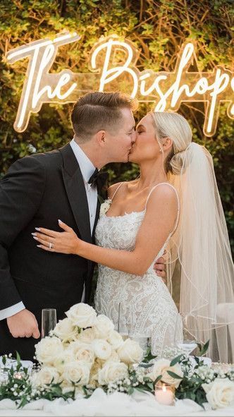 A bride and groom are kissing in front of a neon sign.