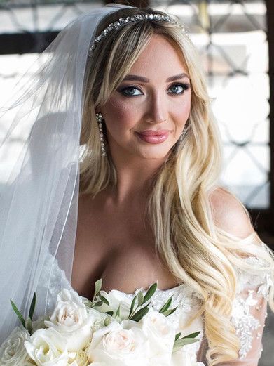 The bride is wearing a veil and holding a bouquet of white roses.