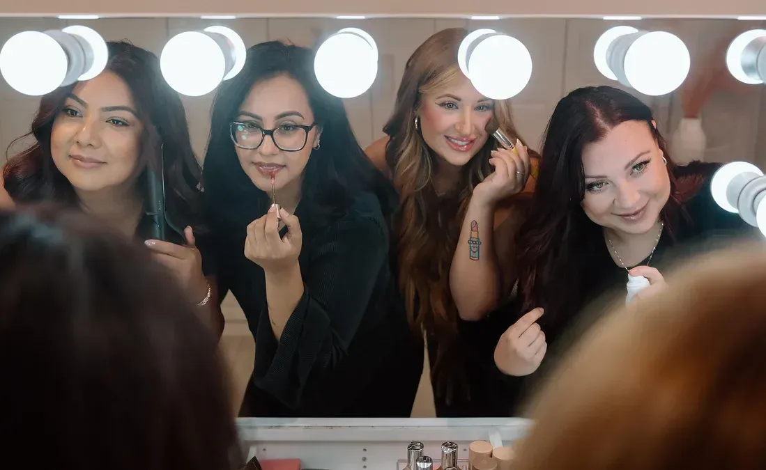 A group of women are applying makeup in front of a mirror.