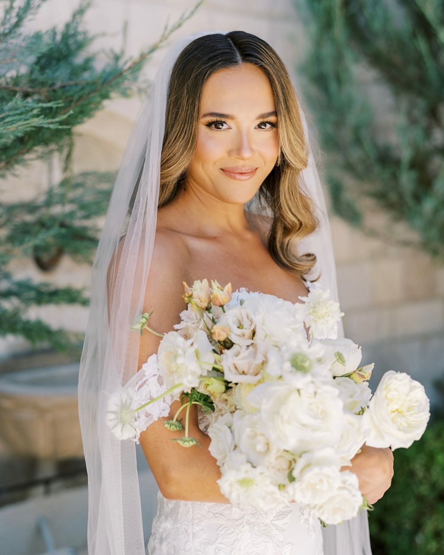 The bride is wearing a veil and holding a bouquet of white flowers.