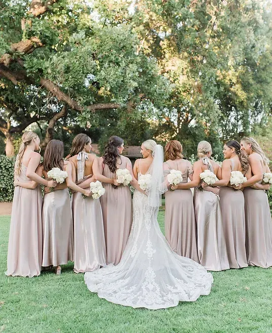 A bride and her bridesmaids are posing for a picture in a field.