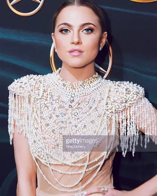 A woman is wearing a white dress with pearls and fringe.