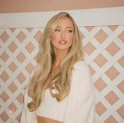 A woman with long blonde hair is standing in front of a white lattice wall.