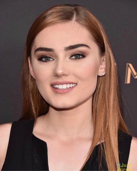 A woman with long red hair is smiling and wearing a black dress