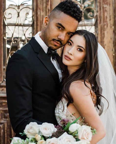 A bride and groom are posing for a picture while the bride is holding a bouquet of flowers.