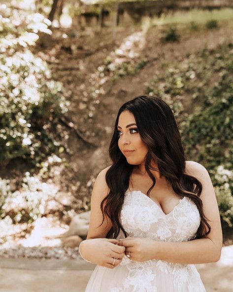 A woman in a white wedding dress is standing in the woods.
