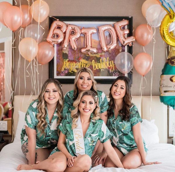 A group of women are sitting on a bed with balloons and a sign that says bride