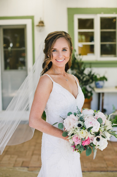 A bride in a white dress and veil is holding a bouquet of flowers.