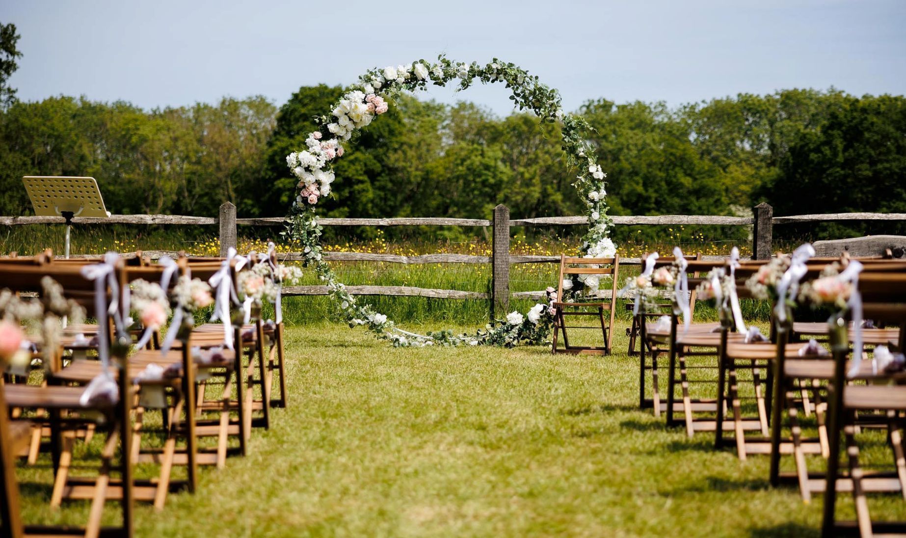 A row of wooden chairs are lined up in a grassy field for a wedding ceremony.
