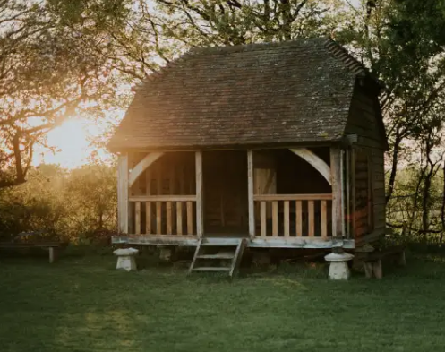 A small wooden house with a porch in the middle of a field.