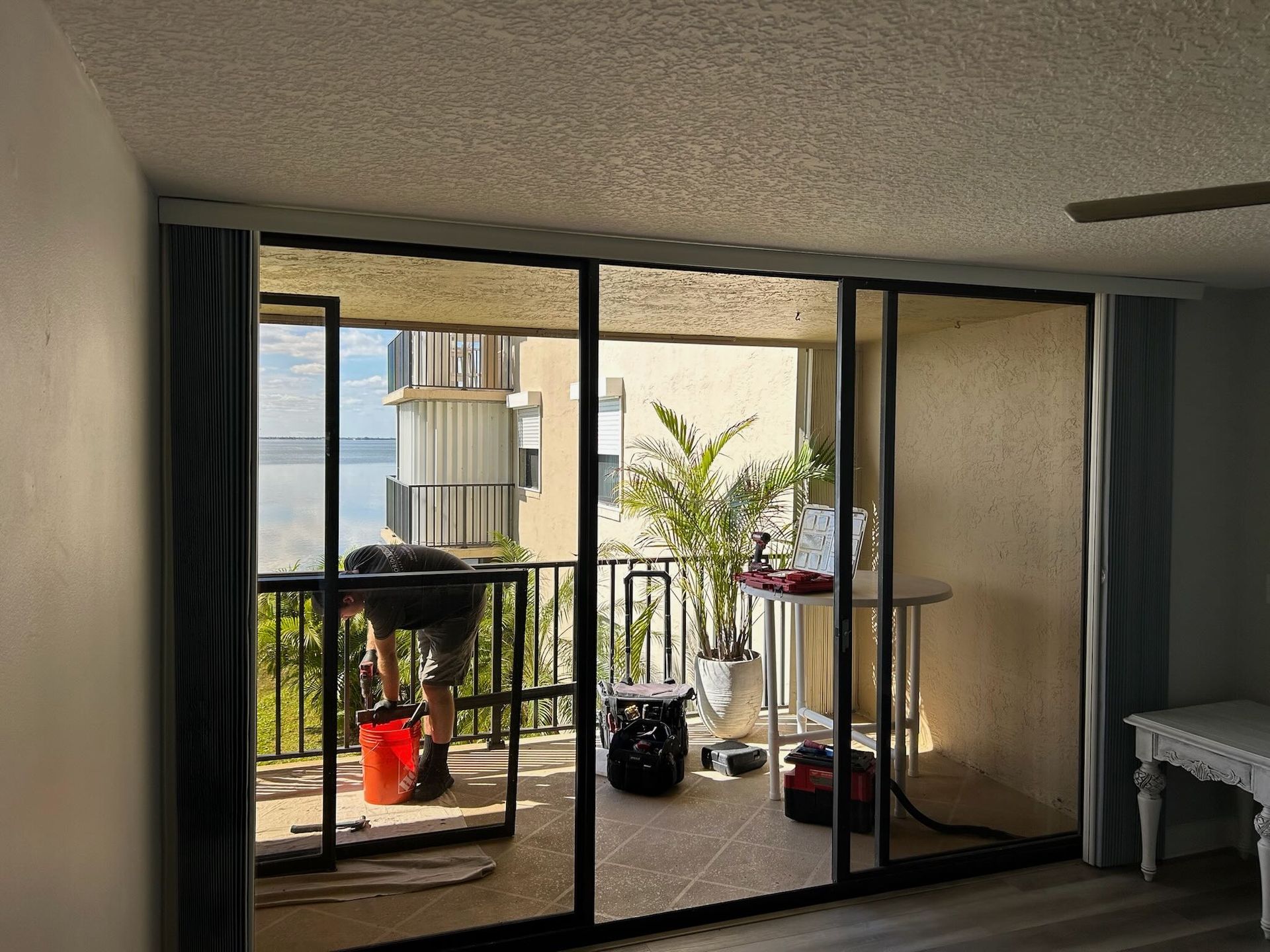 a man repairing a stuck sliding glass door on a balcony of a condo overlooking the water