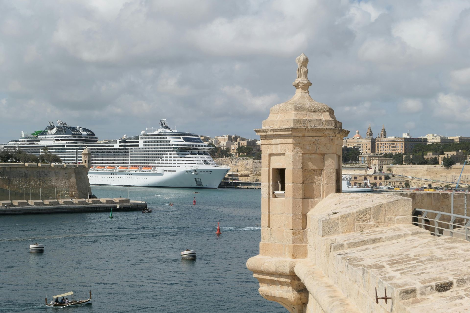 Harbor view with cruise ship and stone fort in Malta. Blue water, cloudy sky.