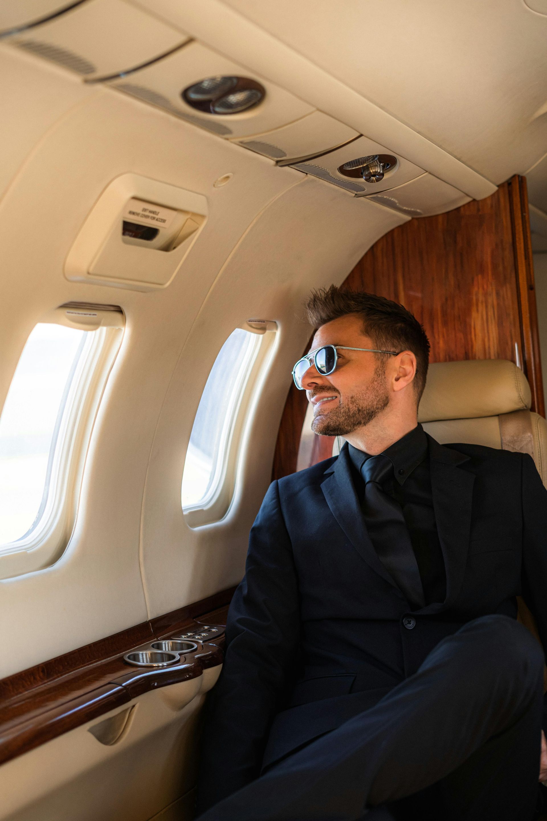Man in sunglasses and suit looks out of a private jet window.