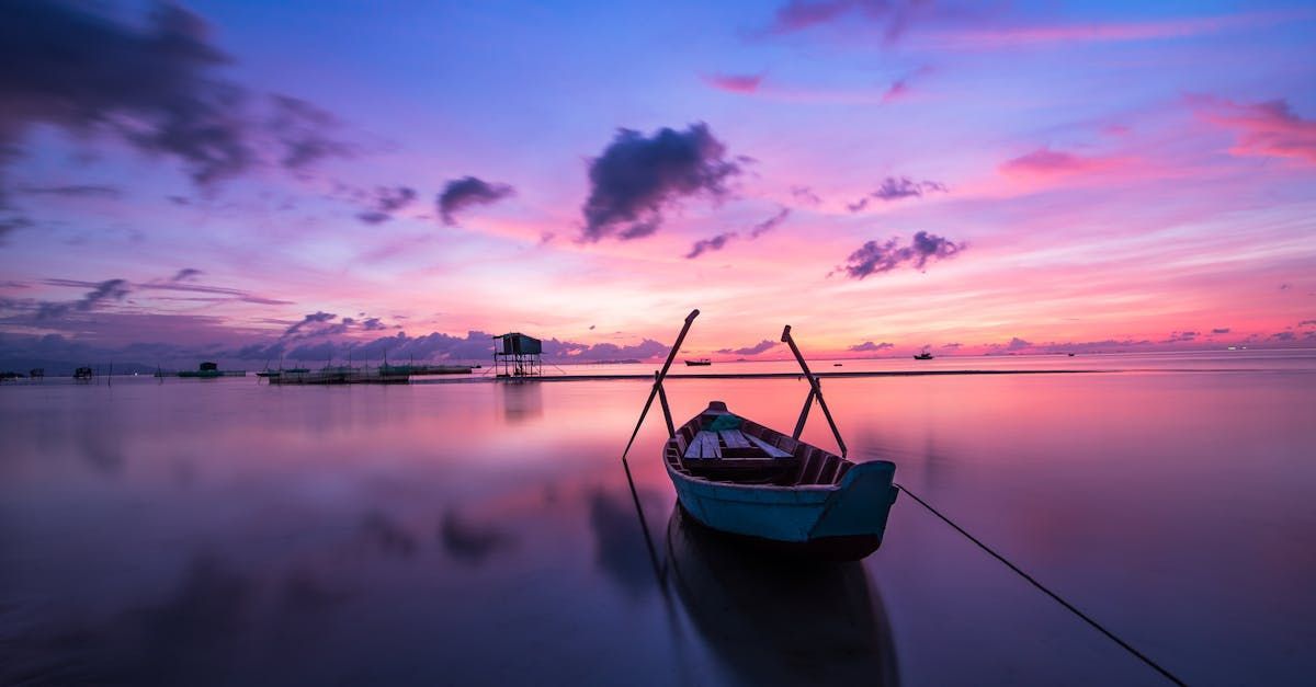 Boat floats in calm water at sunset with vibrant pink and purple sky on a luxury vacation.